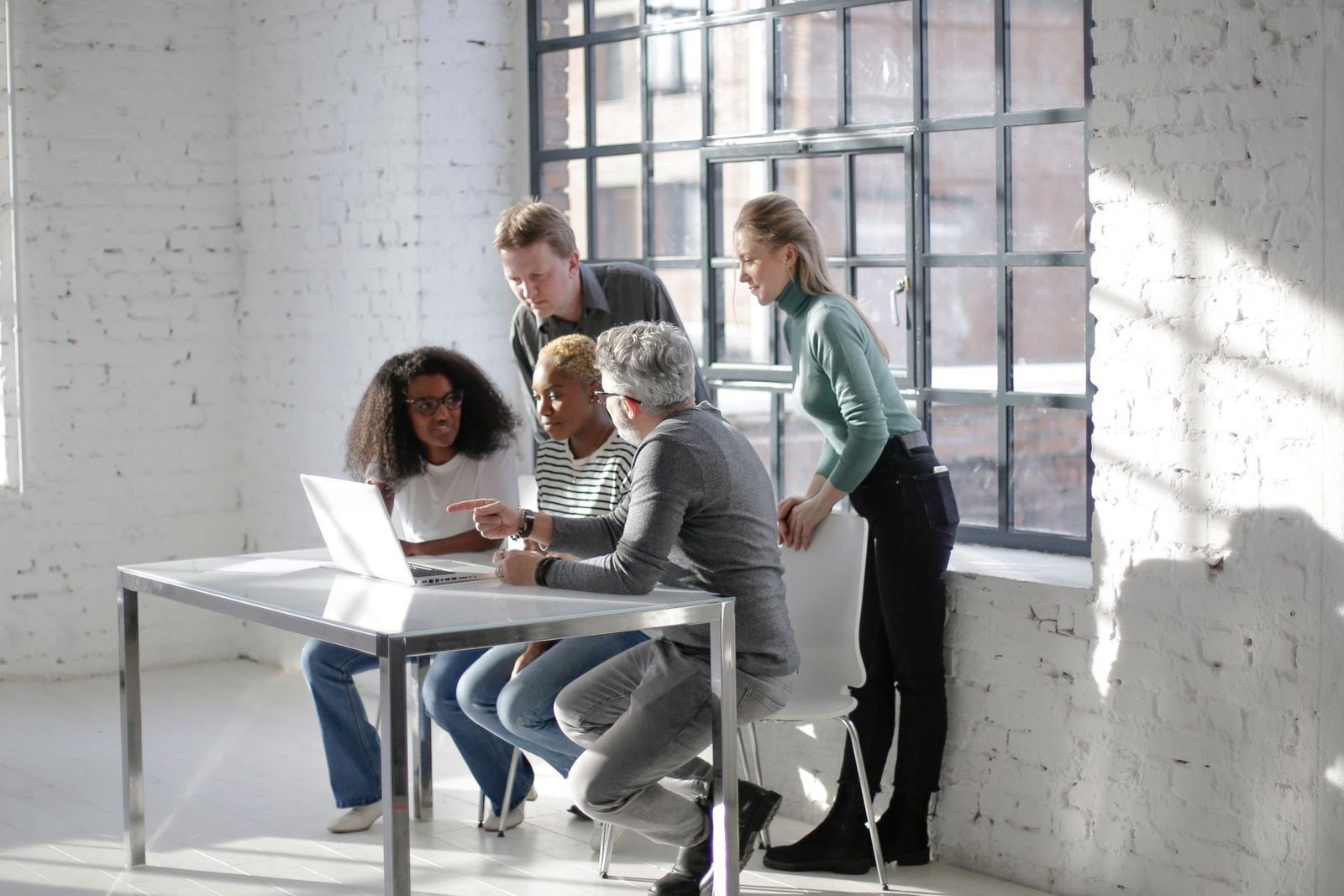 A diverse group of professionals collaborating around a laptop in a bright office